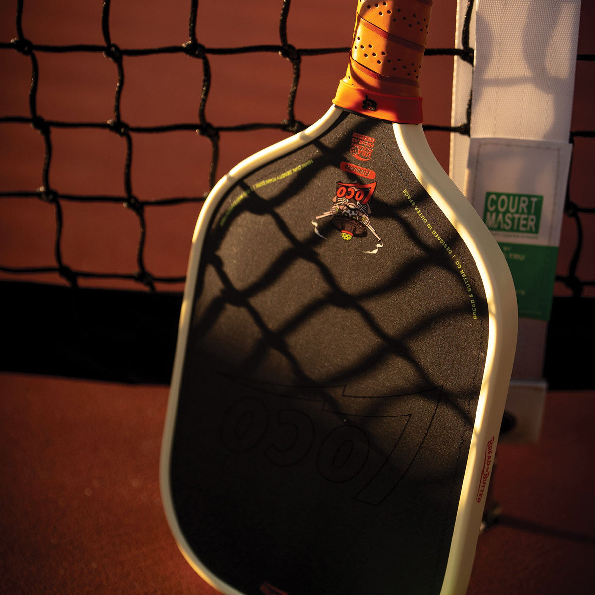 Bread & Butter Loco Elongated Pickleball Paddle - Cream/Tan, angled view at net
