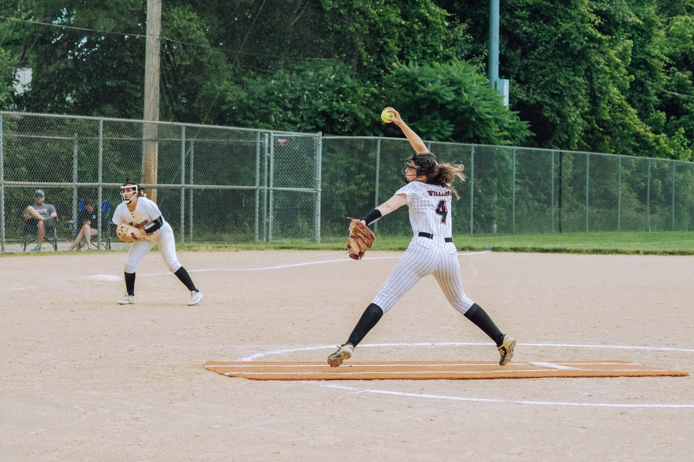 Fastpitch softball pitcher in pinstripe uniform in windmill delivery